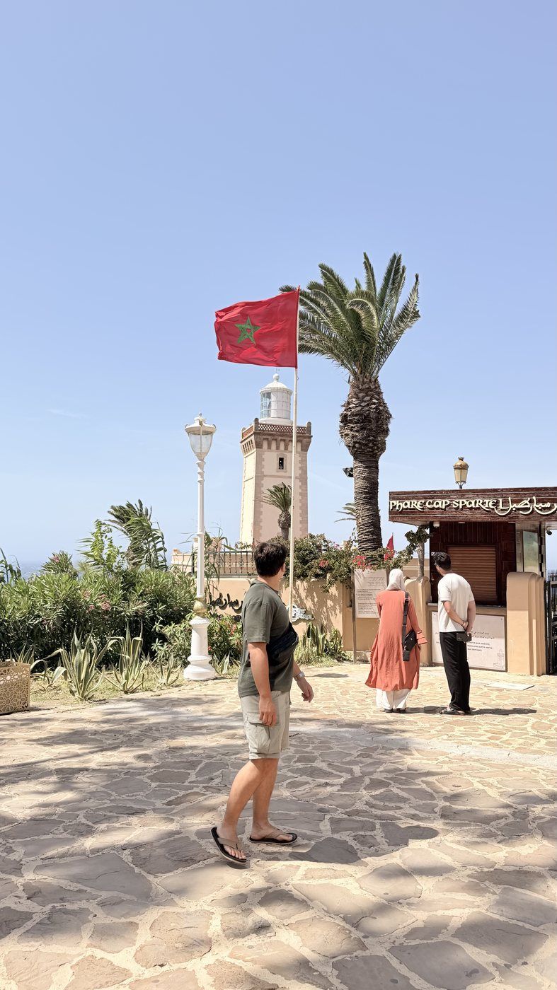 Taras caminando bajo una bandera de Marruecos junto al faro del cabo Espartel