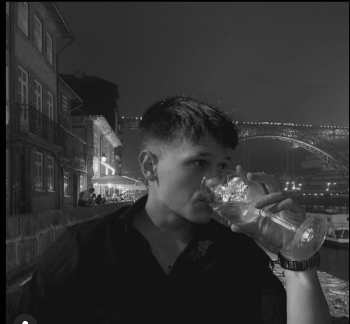 Taras bebiendo una copa de vino de noche, con el puente Don Luis I de Oporto detrás, en blanco y negro